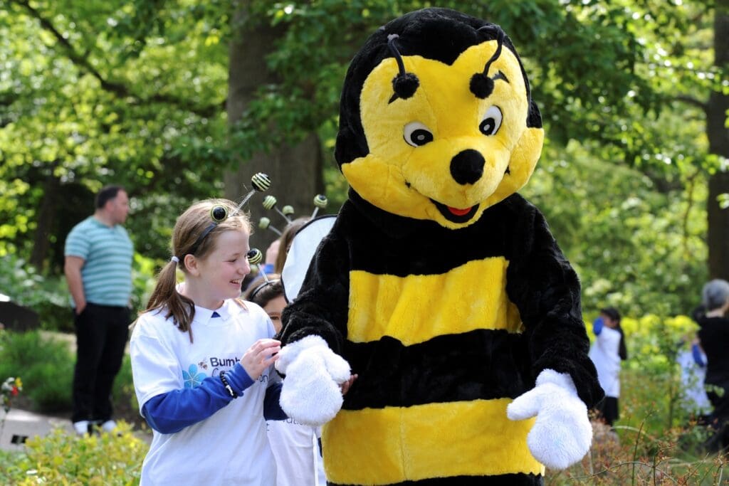 A young girl holding the hand of a bumblebee costume.