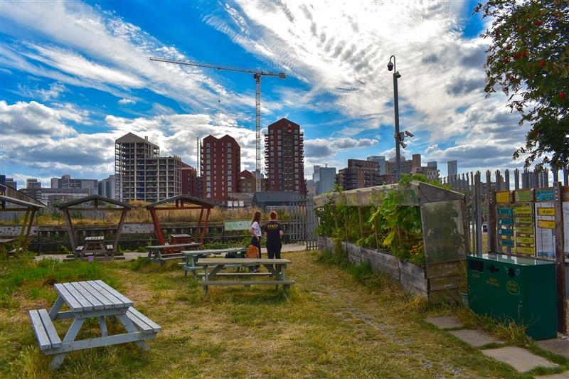 Two people in greenspace with view of London and high rise blocks with sun and cloud